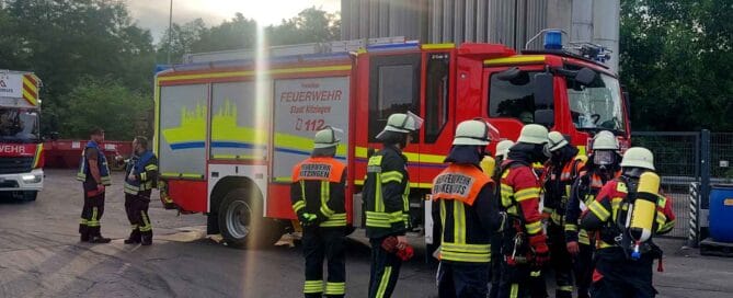 Mehrere Feuerwehrleute in Einsatzkleidung stehen vor einem Feuerwehrauto, einige tragen Atemschutzgeräte.