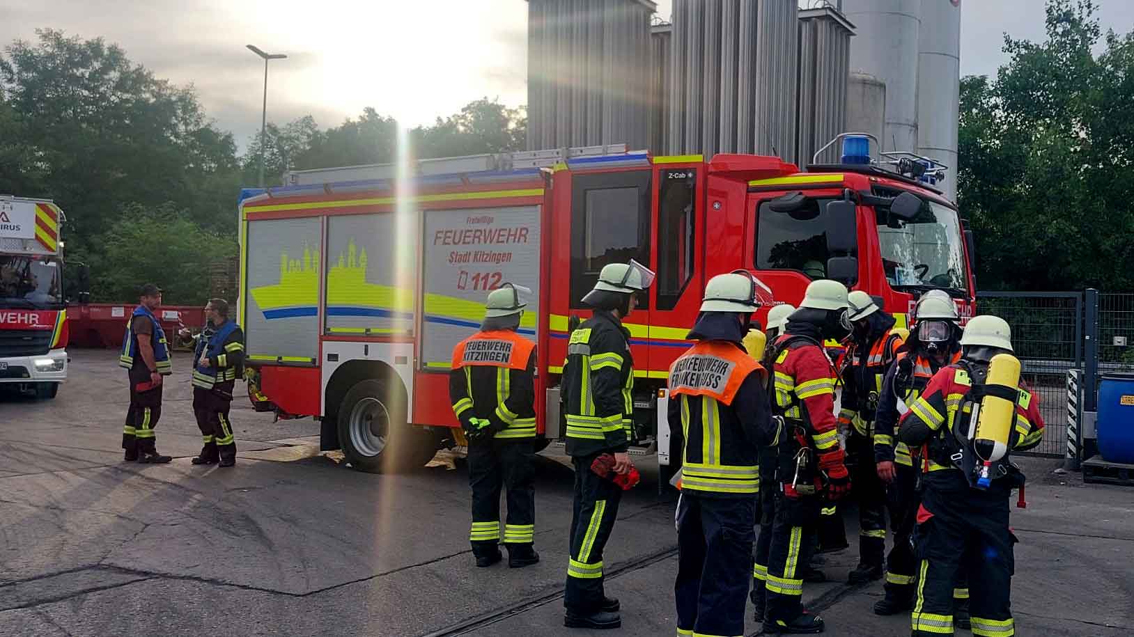 Mehrere Feuerwehrleute in Einsatzkleidung stehen vor einem Feuerwehrauto, einige tragen Atemschutzgeräte.