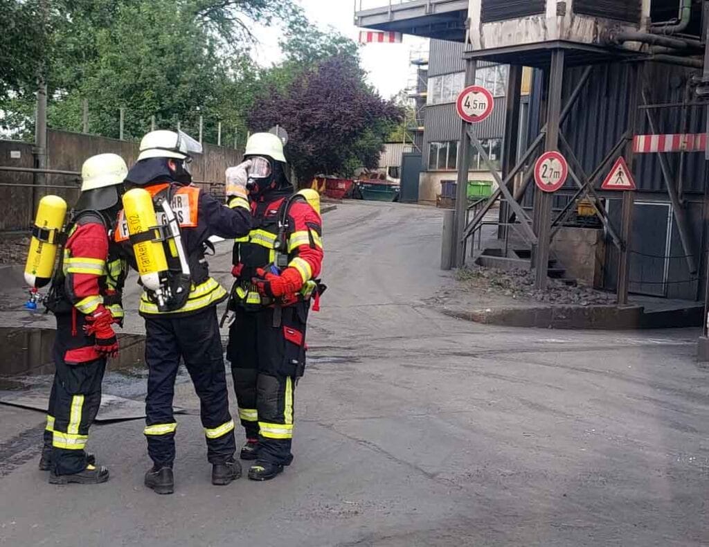 Drei Feuerwehrleute mit Atemschutzgeräten stehen im Gespräch.