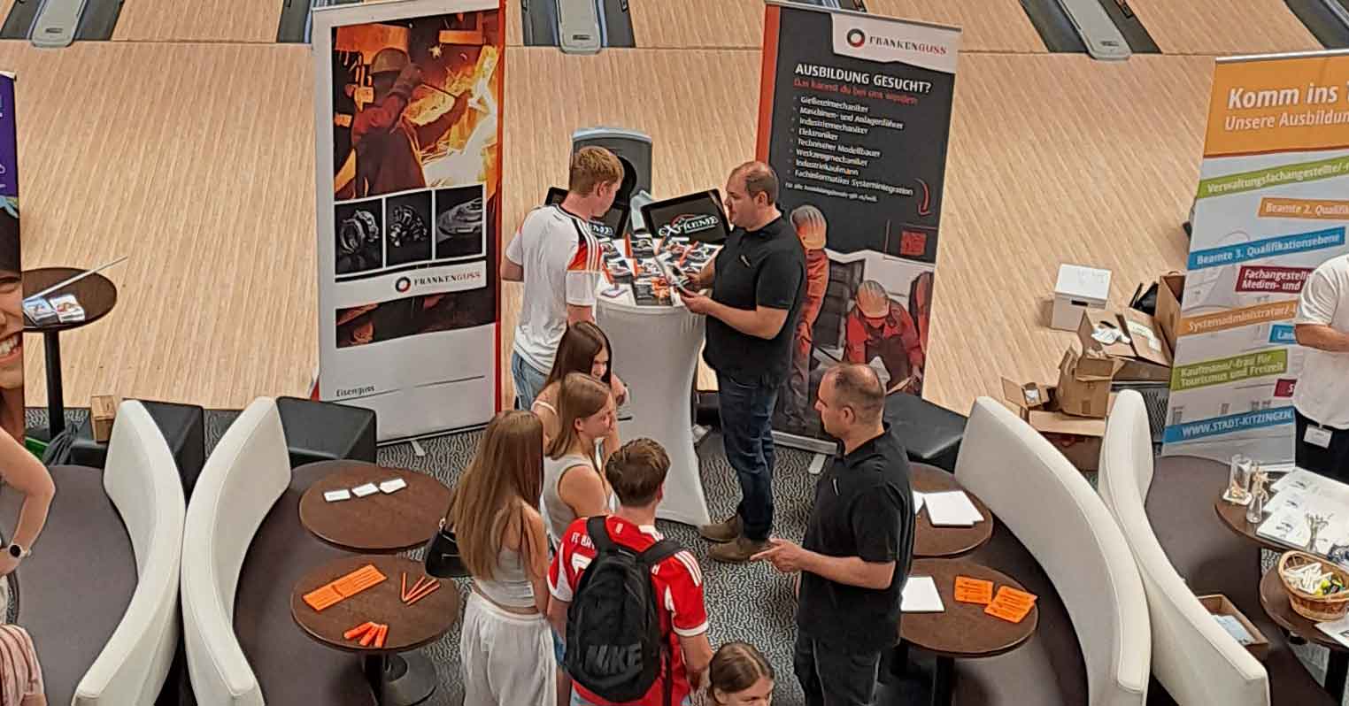 Messestand von Franken Guss bei der AzubiXperience von oben. Zwei Mitarbeiter sind im Gespräch mit mehreren Jugendlichen.
