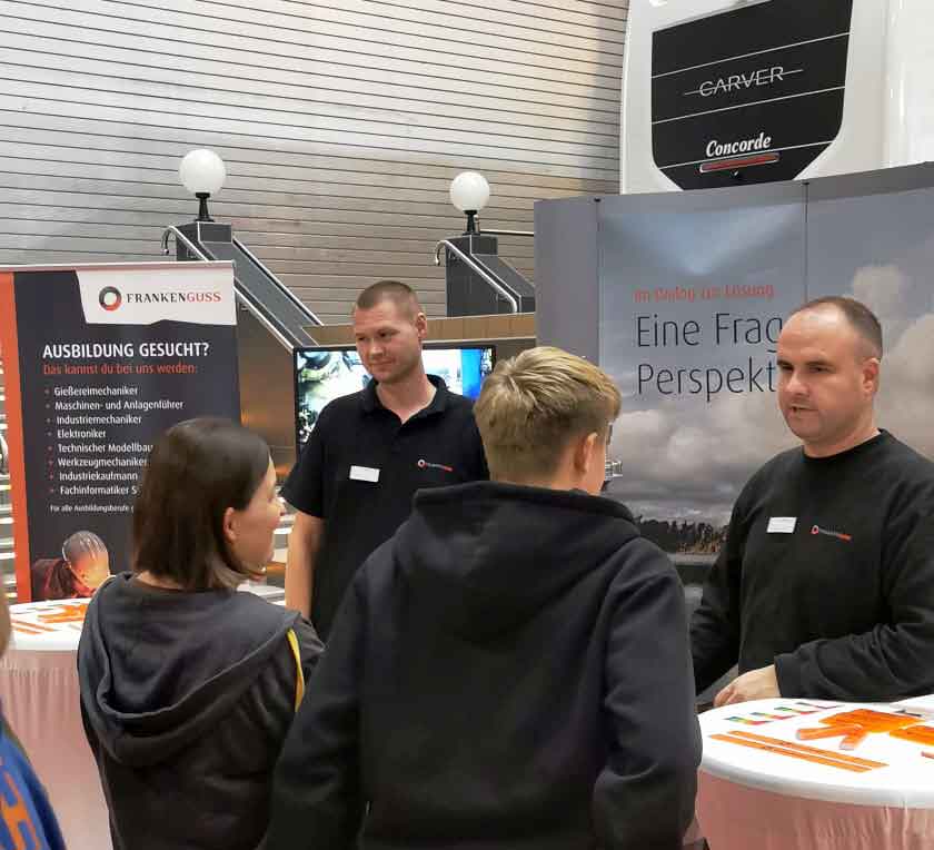 Zwei Mitarbeiter von Franken Guss sprechen am Messestand mit einer Frau und einem Jugendlichen.