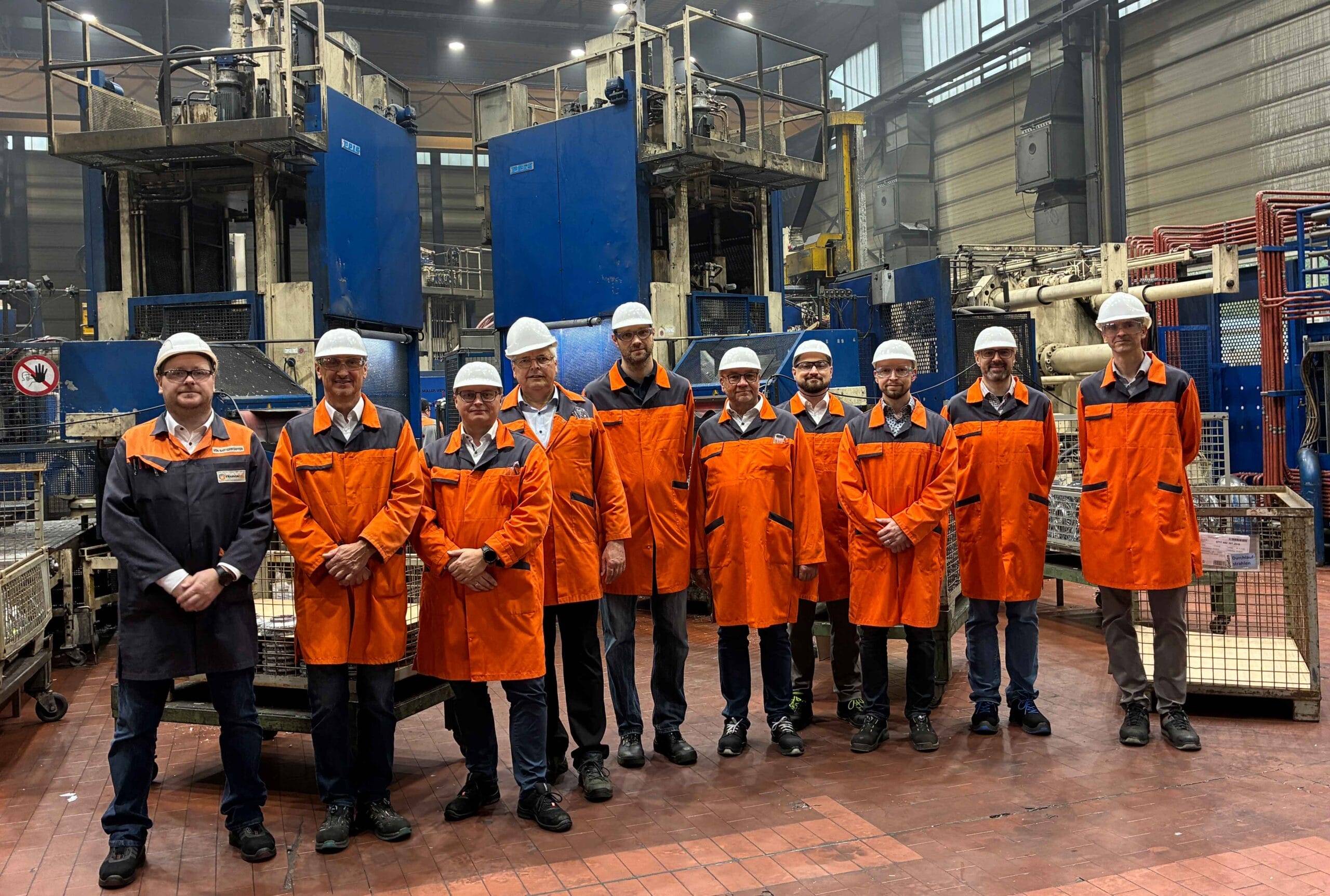 Gruppenfoto des Fachausschusses "Druckguss, intern" vor zwei Druckgussmaschinen bei Franken Guss.